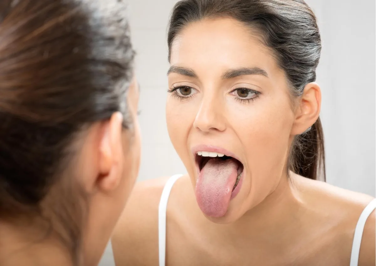 Woman examining her tongue in a mirror for visible signs of oral thrush.